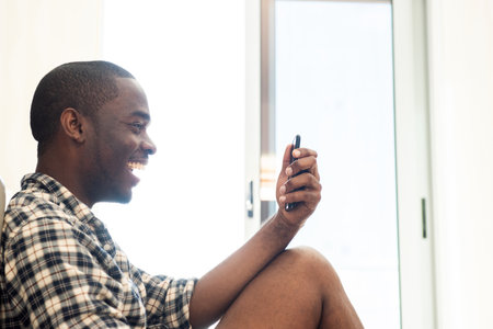 Portrait african American man sitting on floor at home looking at cellphone