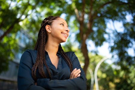 Portrait of smiling young african american woman with mobile phone and luggage walking on city...