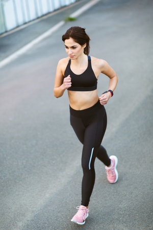 Full body portrait of active young woman running sprinting outdoors in morningの写真素材
