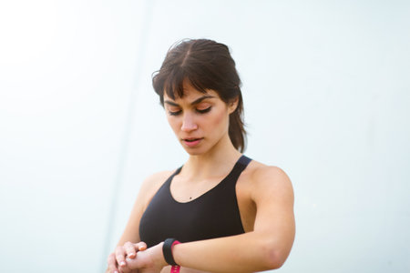 Close up portrait of fit female runner using smart watch to monitor her performance outside against...