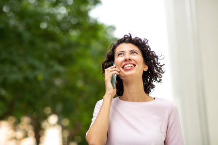 Cheerful young woman looking away while using mobile phone outdoors in city