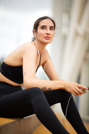 Portrait of caucasian young woman sitting on steps outside in the city listening to music with...