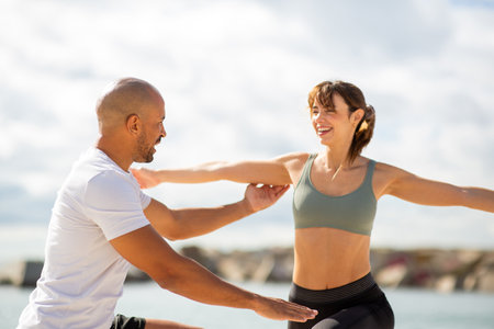 Two fitness enthusiasts engaging in partner stretching exercises with a beautiful coastal backdropの写真素材