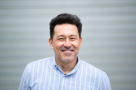Close-up portrait of smiling mature latin man standing against grey background