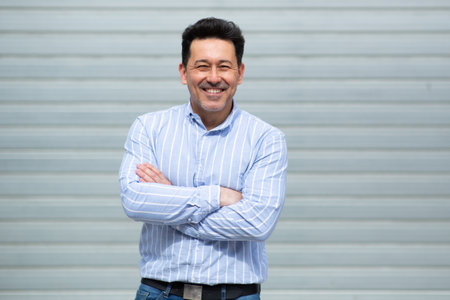 Portrait of mature latin man standing with arms crossed against grey background