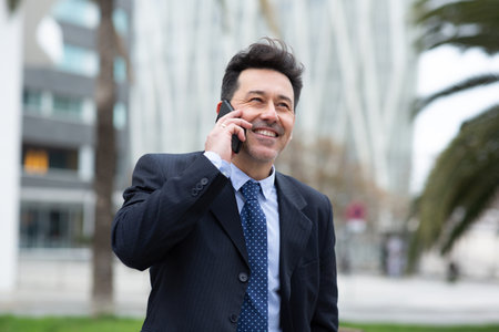 Portrait of happy mature businessman talking on cellphone and smiling walking outside in the cityの写真素材