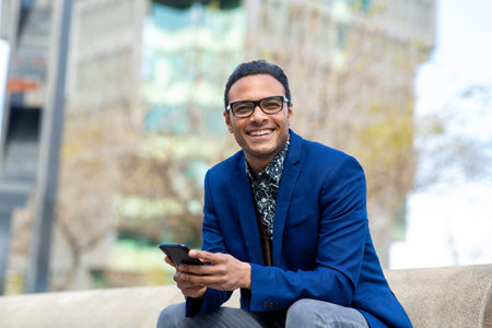 Portrait of good looking young black businessman sitting outside with cell phoneの写真素材