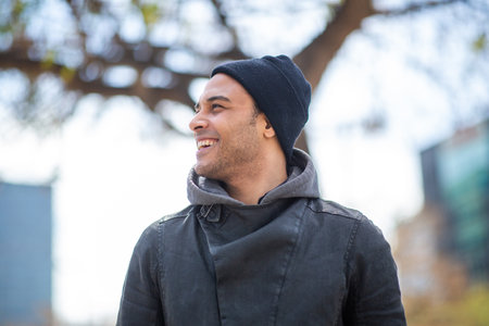 Close up portrait of handsome young african man in black jacket and hat looking away and smiling...