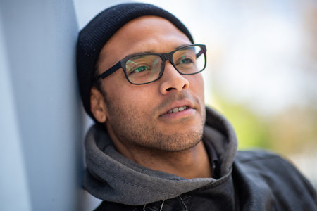 Close up portrait of african american man with eyeglasses leaning to a wall looking away and thinkingの写真素材