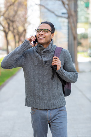 Portrait of handsome young mixed race man talking on mobile phone with bag in the cityの写真素材