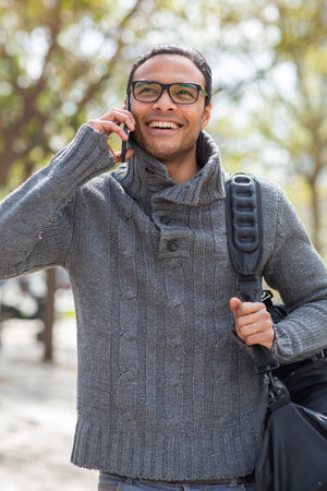 Portrait of stylish young man talking on cell phone carrying bag outsideの写真素材
