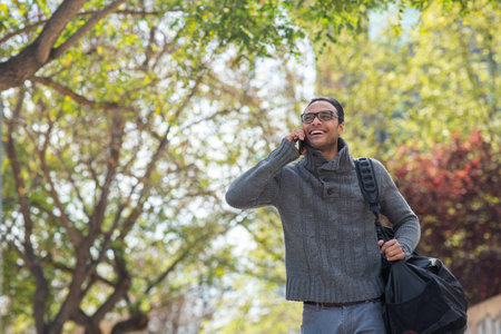 Portrait of smiling african man with bag walking outside and talking on cell phoneの写真素材