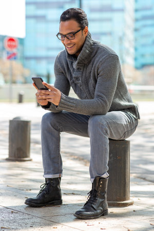 Portrait of young african man sitting outside using mobile phone in the cityの写真素材