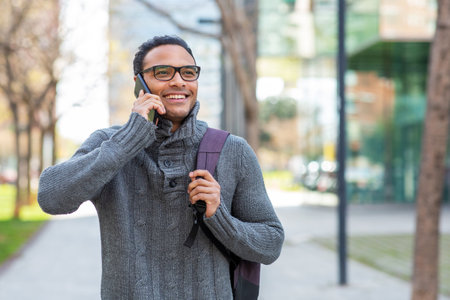 Portrait of attractive young african man with bag walking outside and talking on phoneの写真素材