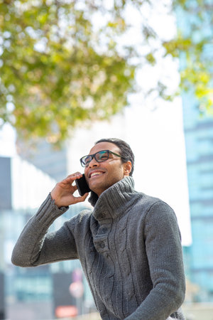 Portrait of cool young african man wearing sweater talking on mobile phone walking outside on a winter dayの写真素材