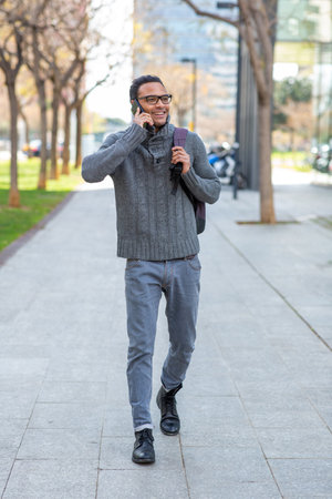 Full body portrait of handsome young black man talking on cell phone with bag in the cityの写真素材