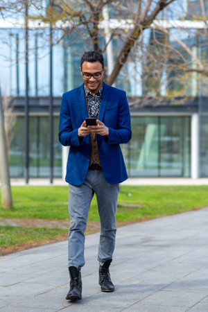 Full length portrait of fashionable young man using cell phone while walking in cityの写真素材