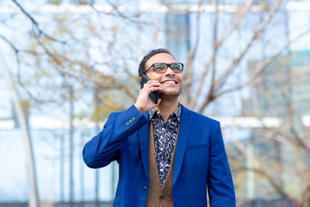 Portrait of stylish young businessman talking on cell phone walking outside in cityの写真素材