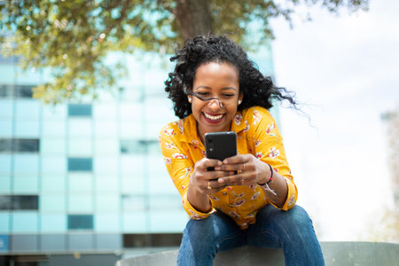 Portrait of pretty young latin woman sitting outside and using cell phoneの写真素材