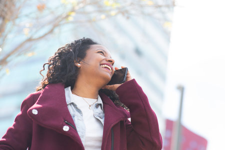 Portrait of beautiful young woman in winter coat smiling and talking on phone outsideの写真素材