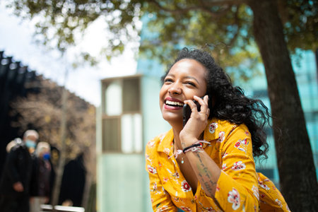 Portrait of cheerful young mixed race woman talking on cell phone outdoors