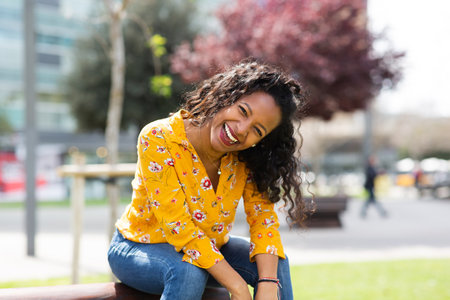 Portrait of attractive young african woman laughing while sitting outside in the cityの写真素材