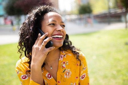 Close up portrait of laughing young african american woman talking on mobile phone outsideの写真素材