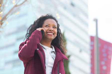Portrait of smiling young african woman talking on cellphone outside in the cityの写真素材
