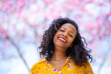 Close up portrait of happy african woman in spring standing against blooming cherry tree