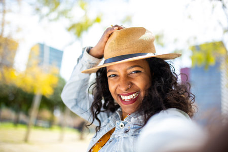Selfie portrait of beautiful young african woman with hat smiling outdoors