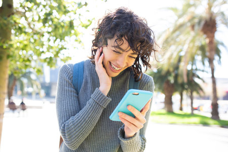 Close-up portrait of pretty young woman looking at cellphone and smiling while walking outside in the cityの写真素材