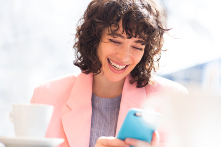 Close-up portrait of beautiful young lady reading text message on her mobile phone sitting at outdoor cafe in the cityの写真素材