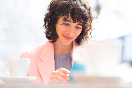 Close-up portrait of beautiful young businesswoman reading text message on her mobile phone sitting at outdoor cafeの写真素材