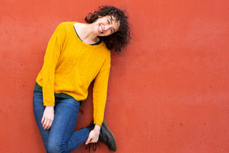 Portrait of stylish young woman posing against red background looking at camera and smiling