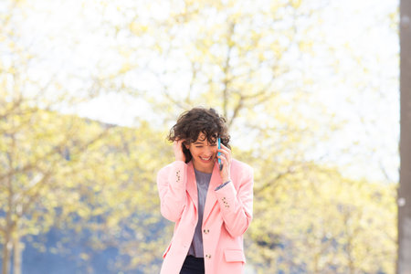 Portrait of cheerful young woman talking on cellphone walking outsideの写真素材