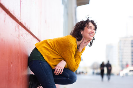 Side portrait of young woman bending over looking away and smiling outdoorsの写真素材