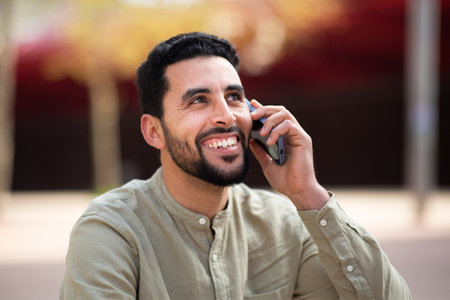 Close up portrait of smiling young arabic guy talking on cell phone outsideの写真素材