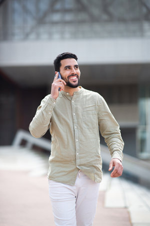 Portrait of young arabic man walking outside and talking on cellphoneの写真素材