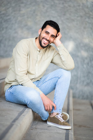Portrait of smiling young arabic man sitting on steps looking at cameraの写真素材
