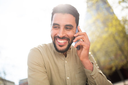Close up portrait of smiling young arabic man talking on cell phone outside on a sunny dayの写真素材
