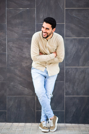 Full body portrait of cheerful young guy standing against black wall with arms crossed looking awayの写真素材