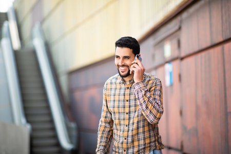 Portrait of handsome young arab man walking outside and talking on mobile phoneの写真素材