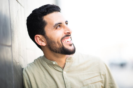 Close up side portrait of smiling young arabic guy man leaning to a wall and looking awayの写真素材