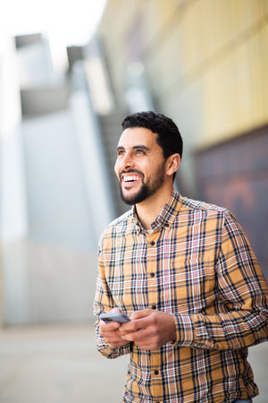 Portrait of handsome young arab man walking outside with mobile phoneの写真素材