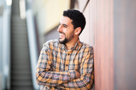 Portrait of handsome middle eastern man standing with his arms crossed against a wall looking away and smilingの写真素材