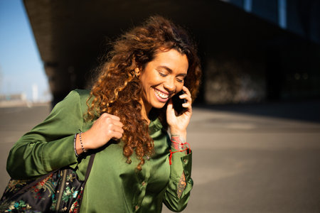 Portrait of smiling mixed race woman talking on mobile phone outdoors in cityの写真素材