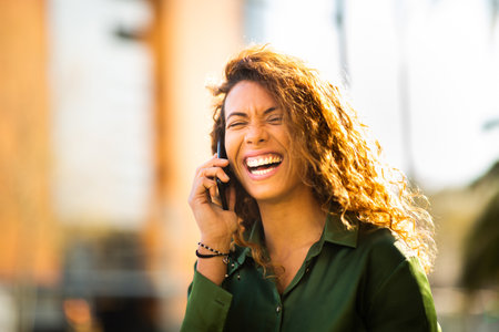 Close up portrait of carefree young mixed race female talking on mobile phone outdoors in cityの写真素材