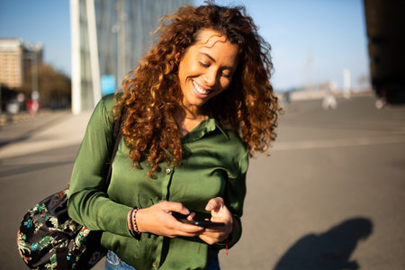 Portrait of attractive young woman walking outside and reading text message on cell phoneの写真素材