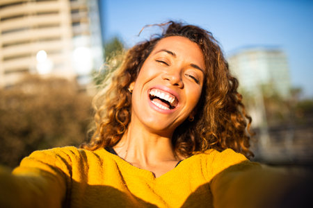 Selfie portrait of cheerful young latin woman outside with curly hairの写真素材