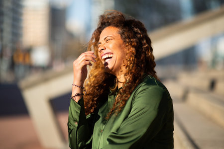 Portrait of cheerful young latin woman sitting on steps outside and laughingの写真素材